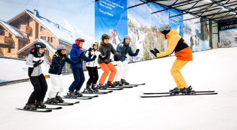 Students receive ski lessons from the ski instructor at the front of a group.