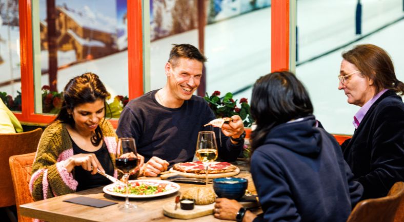 Twee stellen dineren in het café-restaurant van Montana Snowcenter met uitzicht op de piste.